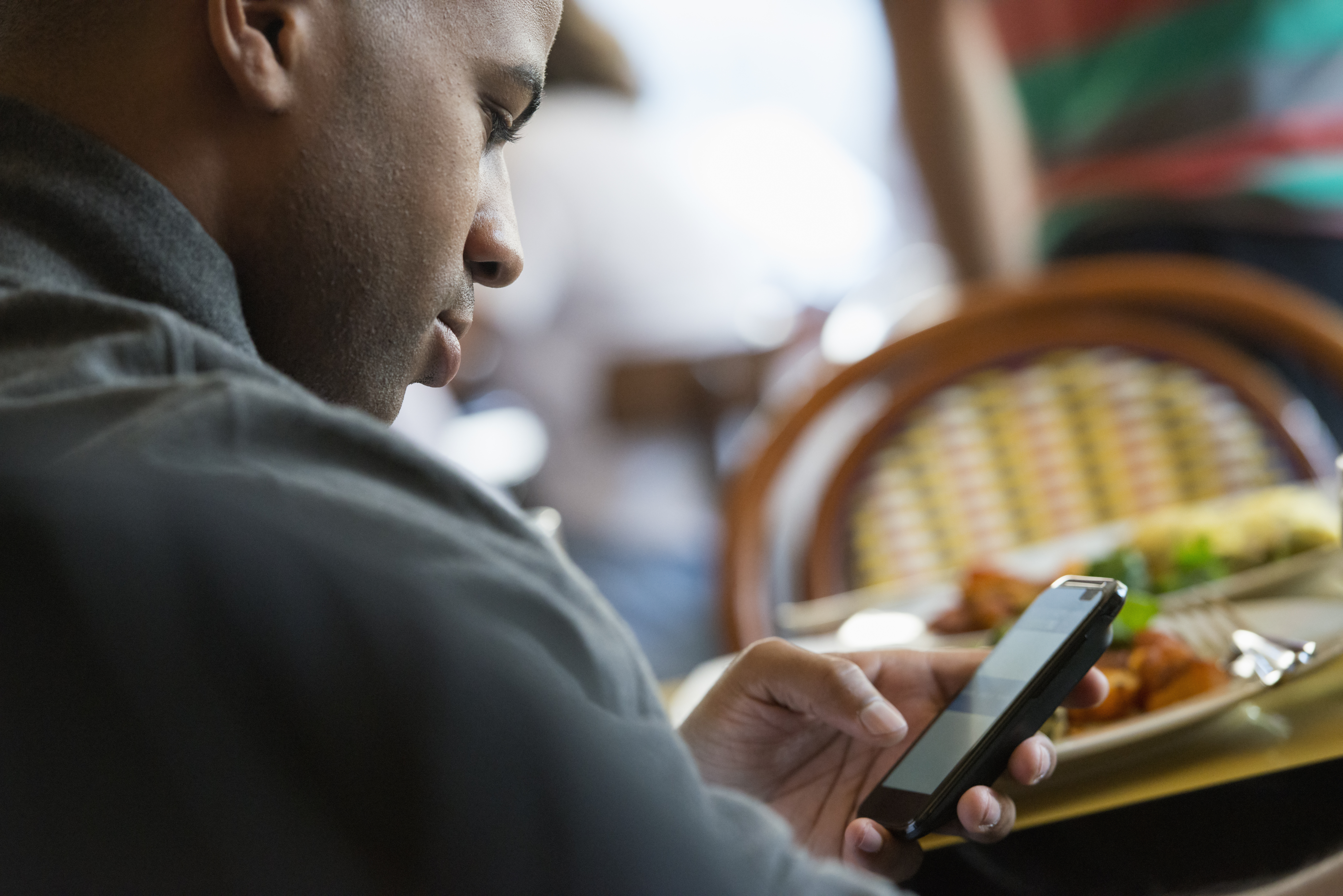 Um homem sentado em um café verificando seu celular para fazer seu cadastro BetMGM Brasil