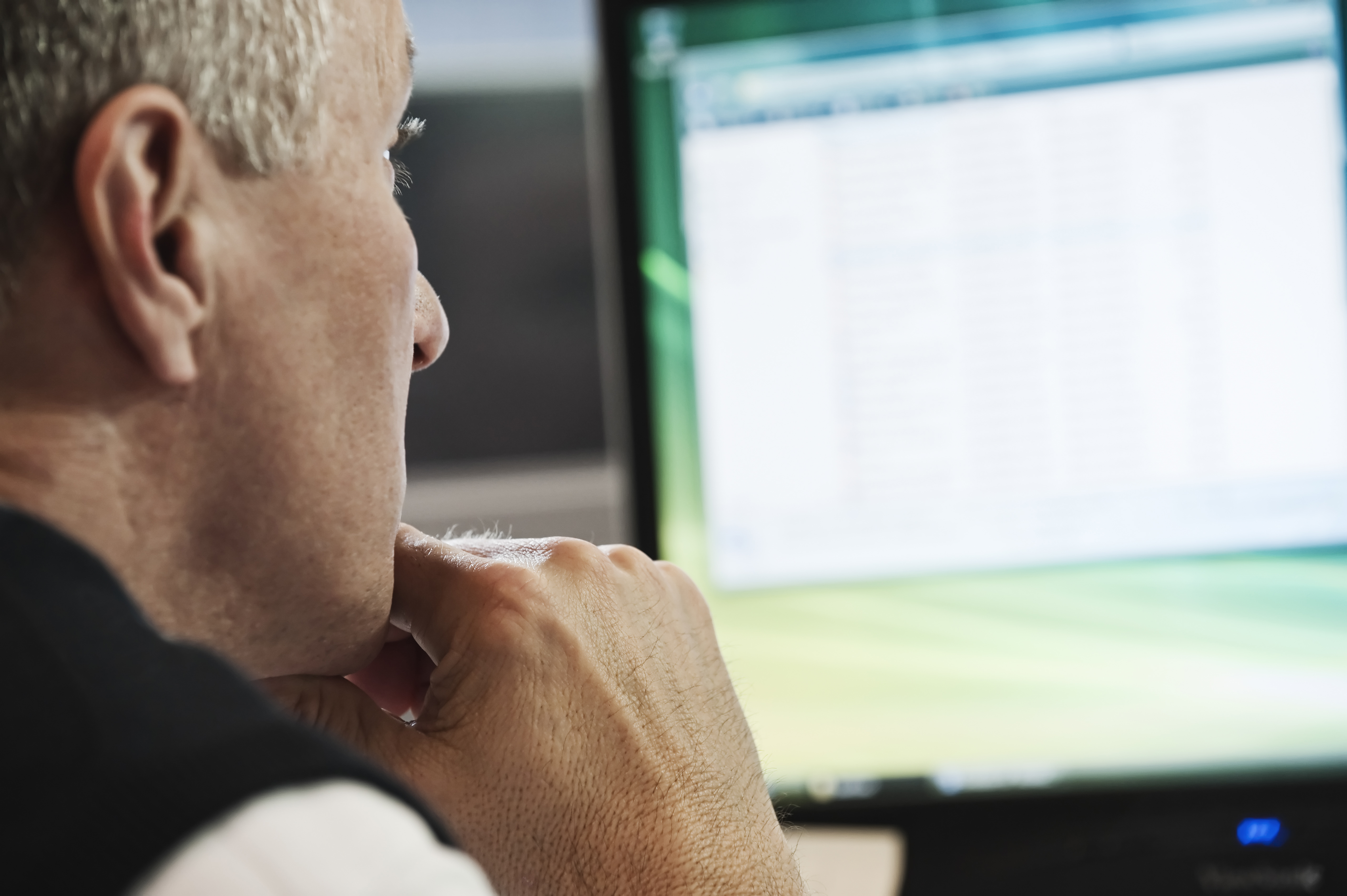 Closeup de um homem adulto caucasiano olhando para um computador desktop, à procura de sites de apostas que aceitam depósito mínimo de 1 real