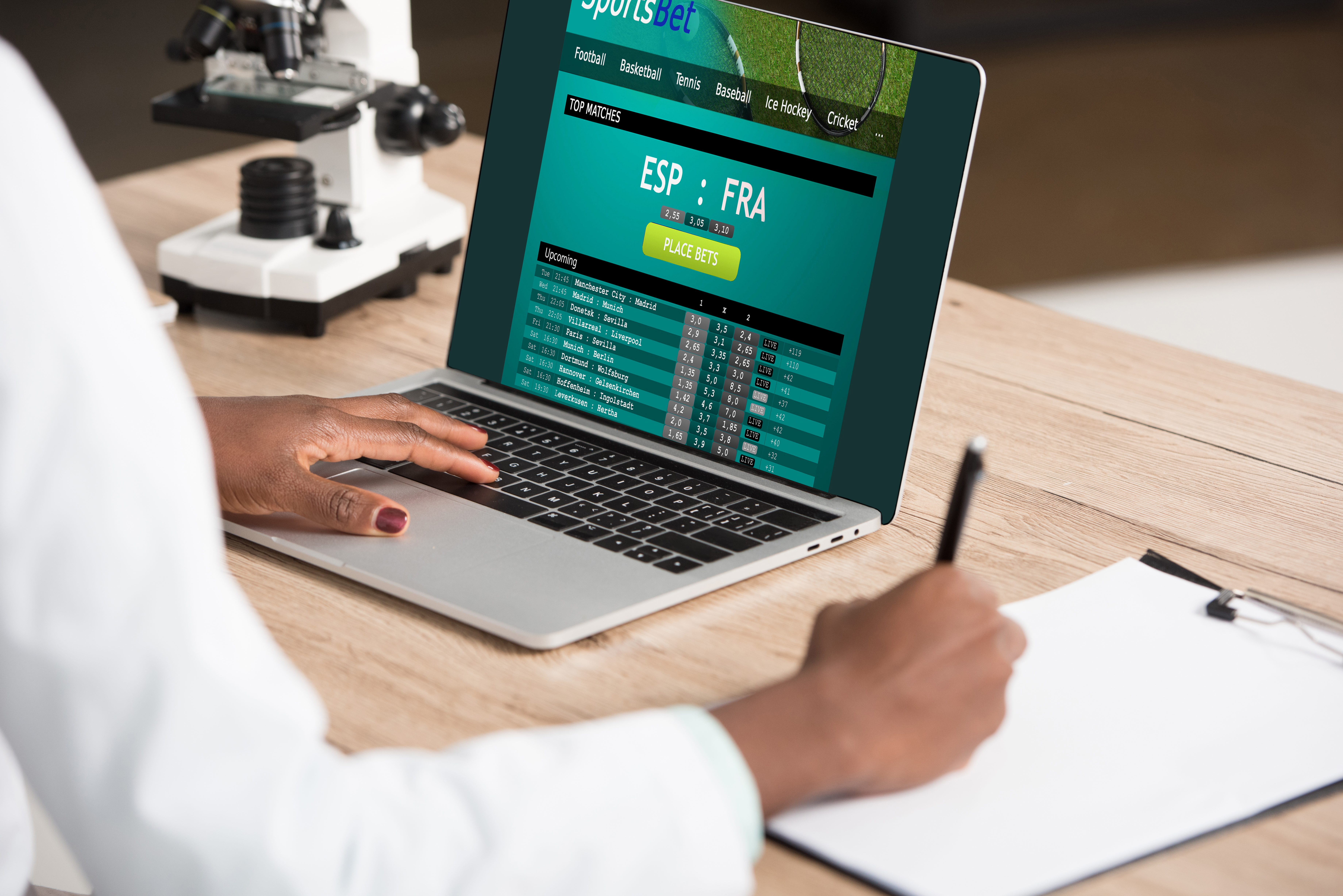 Visão recortada de homem afro-americano usando laptop para acessar site de apostas esportivas e colocar em prática as dicas para apostar ao vivo em futebol em ação, ao mesmo tempo em que faz anotações no caderno ao lado