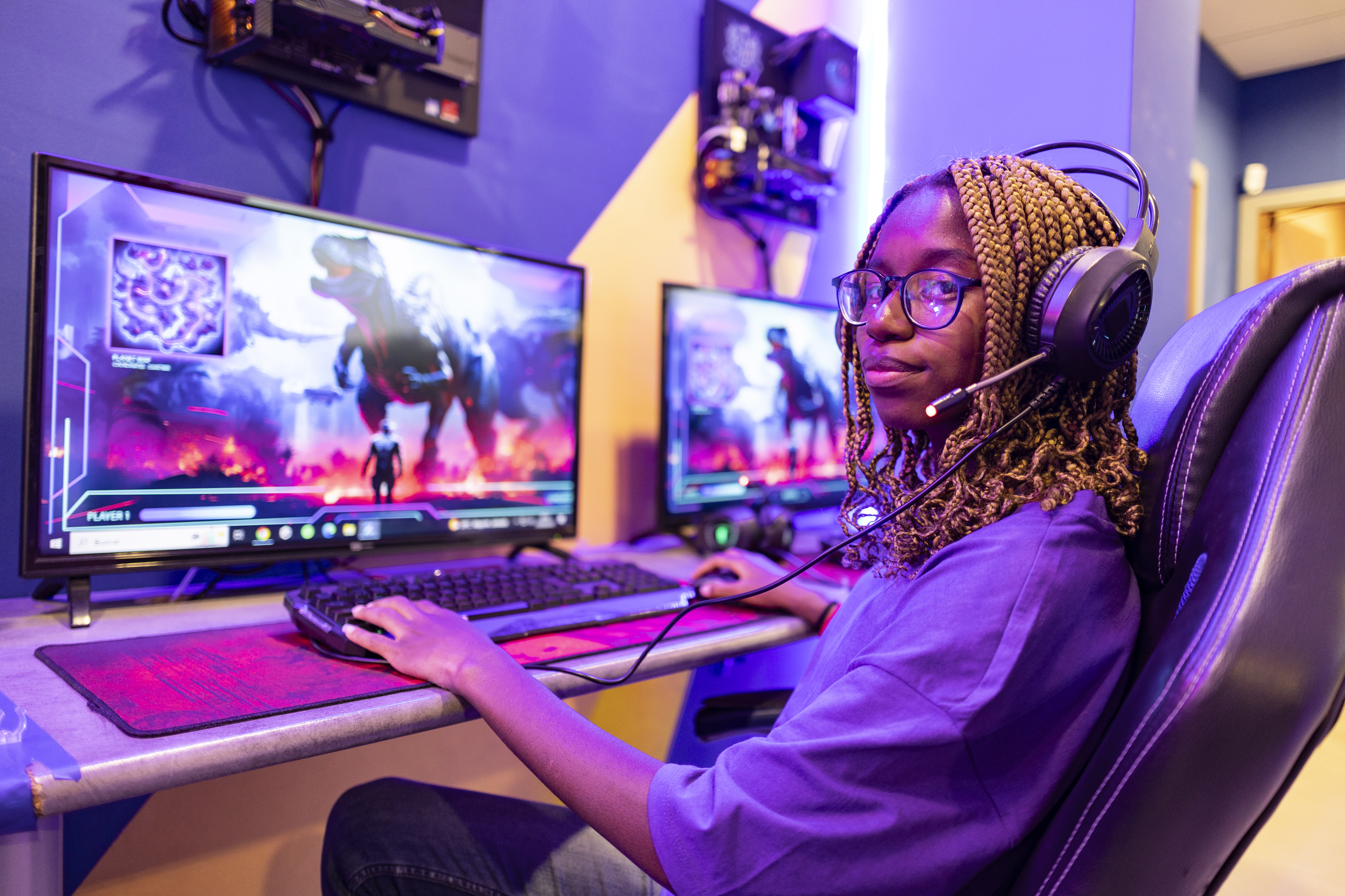 Jovem usando fone de ouvido e jogando um videogame online futurista lutando contra um dinossauro usando seu computador e mouse em uma sala de jogos roxa, representando os jovens que comemoraram o eSports ter sido incluído na lista de esportes autorizados para apostas quota fixa no Brasil.