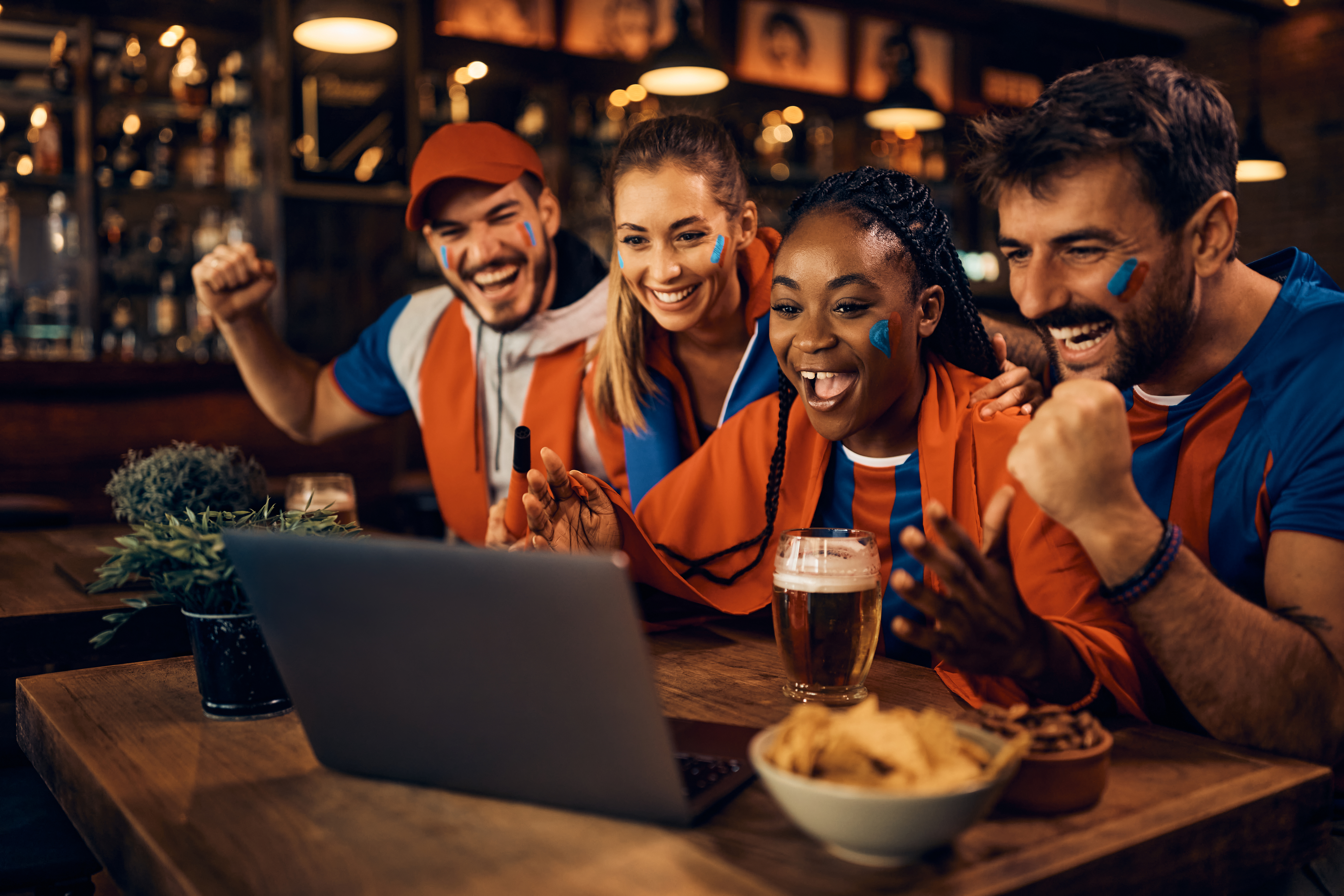 Torcedores comemoram resultado de aposta esportiva enquanto assistem a uma partida pelo computador, representando a emoção e o impacto das odds nas apostas online.